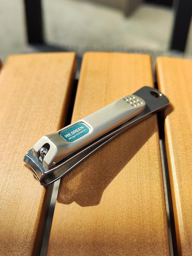 MR.GREEN curved blade stainless steel nail clippers with non-slip lever for precise trimming — lifestyle photo on wooden bench